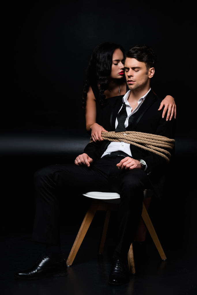 Brunette woman in dress near tied submissive man sitting on chair on black - Stock Photo & Image

By VitalikRadko 4912x7360 px